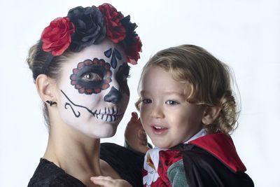 Portrait of mother with face paint carrying son against white background