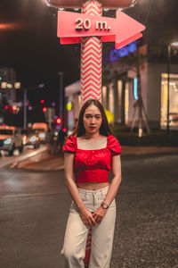 Portrait of young woman standing by pole in city at night