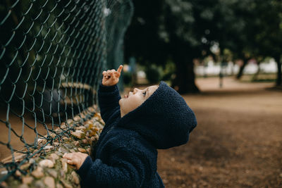 Side view of boy playing with chainlink fence
