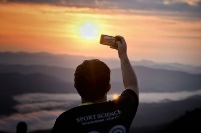 Rear view of man photographing against sky during sunset