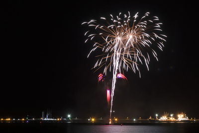 Low angle view of firework display over sea against sky at night