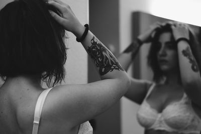 Tattooed woman wearing bra looking in mirror at home