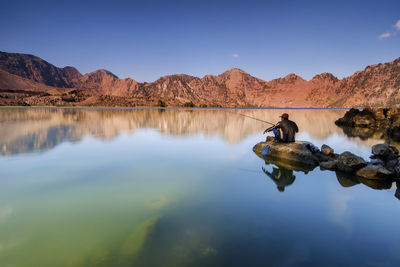 Man on rock by lake against sky