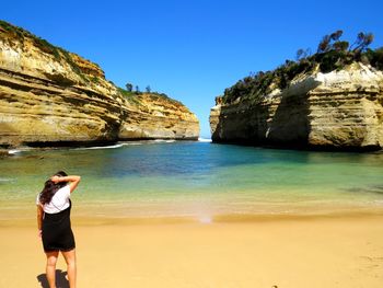 Rear view of woman standing on rock at beach against sky