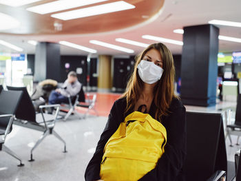 Young woman wearing mask sitting at airport