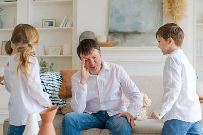 An annoyed father sitting on sofa at home in living room distracted from noise