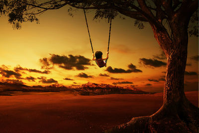 Rear view of girl swinging over land against sky during sunset