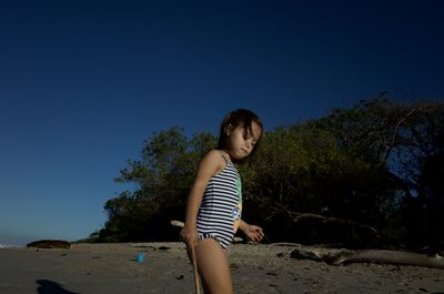 Full length of young woman at beach against clear blue sky