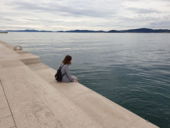 Man sitting on shore against sky