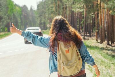 Rear view of backpacker hitchhiking on road in forest