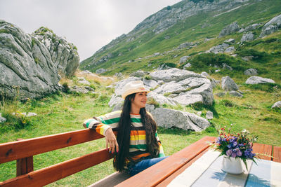 Woman wearing cowboy hat while sitting at picnic table against mountain