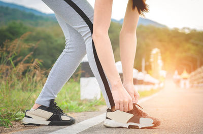 Low section of woman tying shoelace while standing on road