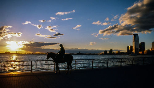 Silhouette man riding horse at beach against sky during sunset