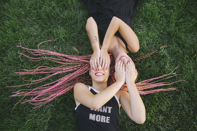 Female friends covering eyes while lying on grass