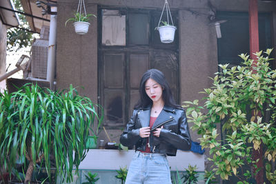 Woman wearing leather jacket standing against house