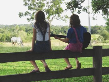 Rear view of siblings sitting on grass against trees