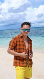 Man wearing sunglasses standing at beach against sky