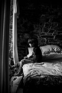 Side view of boy sitting on bed at home