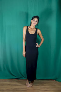 Portrait of standing adult model in black dress against dark green background. 