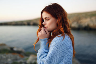 Beautiful young woman looking at sea during sunset
