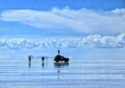 Distant view of silhouette friends at salar de uyuni against cloudy sky