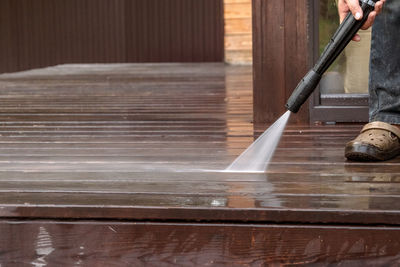 Man cleaning walls and floor with high pressure power washer. washing terrace wood planks and clad