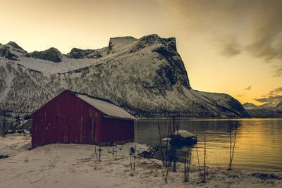 Wooden house on snow against sky during sunset