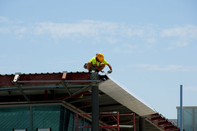 Low angle view of man standing on roof against sky