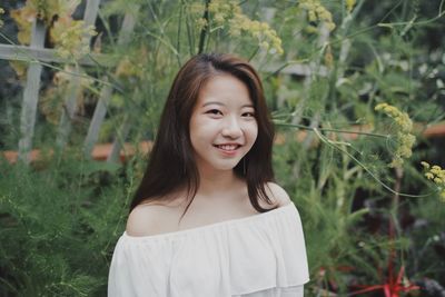 Portrait of smiling young woman by plants at public park