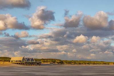 Stilt houses on sand against cloudy sky