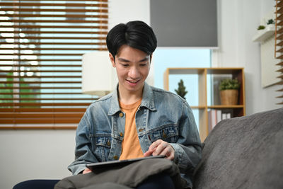 Young man using digital tablet while sitting on sofa at home