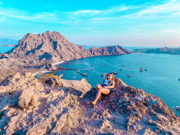 Rear view of person on rock by sea against sky