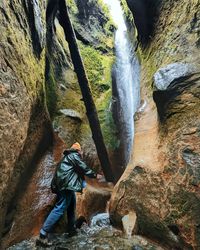 Rear view of woman standing on rock underneath a waterfall