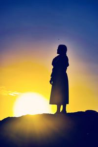 Rear view of silhouette woman standing against sky during sunset