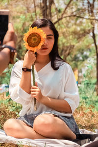 Midsection of woman holding flower while sitting on plant