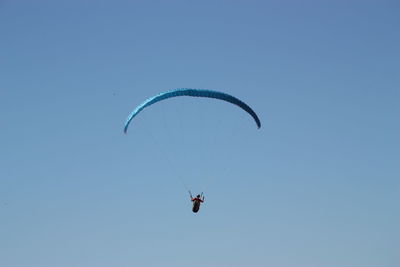 Low angle view of man paragliding against clear blue sky