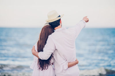 Rear view of man pointing while standing with girlfriend at beach