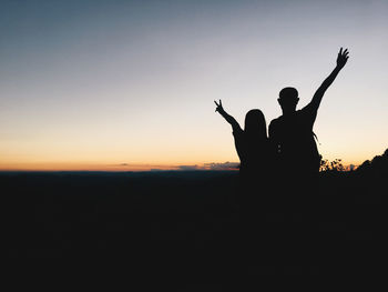 Silhouette woman with arms raised against sky during sunset