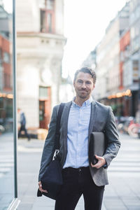 Portrait of smiling mature entrepreneur with bag standing in city