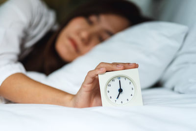 Midsection of woman with alarm clock on bed at home