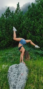 Woman doing handstand on rock against plants