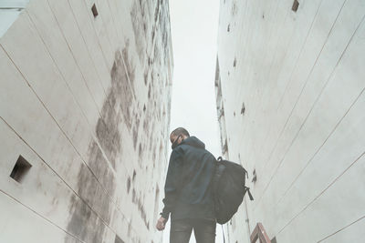 Rear view of man walking by building against sky