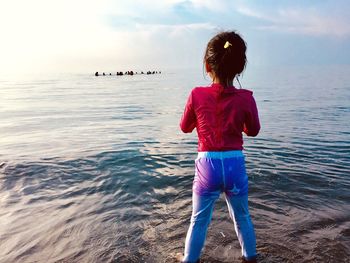 Rear view of woman standing on sea shore against sky