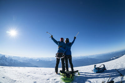 Two happy female mountaineers raise their ice axes in victory