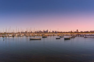 Sailboats moored in harbor against clear sky during sunset