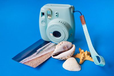 High angle view of camera, seashells and postcard of sea against blue background