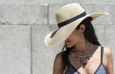 Portrait of young woman wearing hat against wall