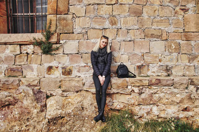 Portrait of smiling young woman sitting against stone wall