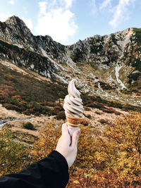 Person holding ice cream on mountain against sky