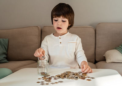 Little toddler boy counting money putting coins into glass jar. kid saving learn financial literacy